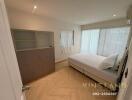 A modern bedroom with a large bed, built-in shelving unit, and natural lighting from wide windows.