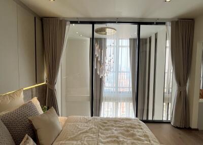 Modern bedroom with a large bed, pillows, a magazine, and a glass door leading to a balcony