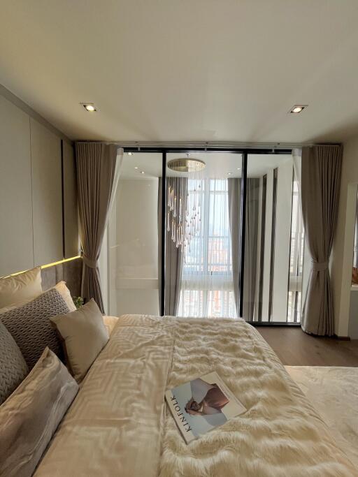 Modern bedroom with a large bed, pillows, a magazine, and a glass door leading to a balcony