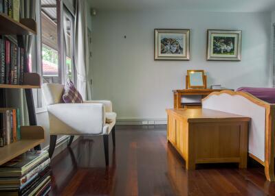 Cozy bedroom with wooden flooring, a chair by the window, bookshelf, and a bed