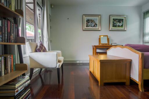 Cozy bedroom with wooden flooring, a chair by the window, bookshelf, and a bed