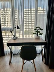 A study area with a desk, chair, lamp, and plant in front of a large window with city view.