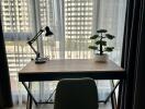 A study area with a desk, chair, lamp, and plant in front of a large window with city view.