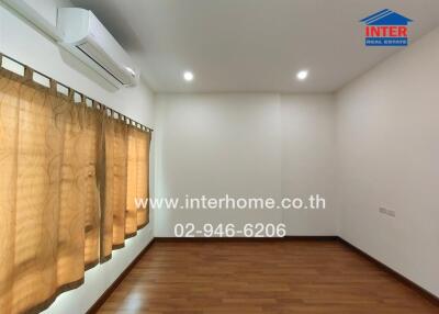 Empty bedroom with hardwood floors, beige curtains, and air conditioning unit.