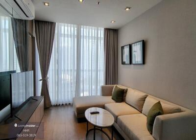 Modern living room with a large sofa and TV, featuring floor-to-ceiling windows and minimalist decor