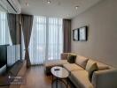 Modern living room with a large sofa and TV, featuring floor-to-ceiling windows and minimalist decor