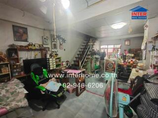 Cluttered living room with a gaming chair, stairs, books, and various personal items.