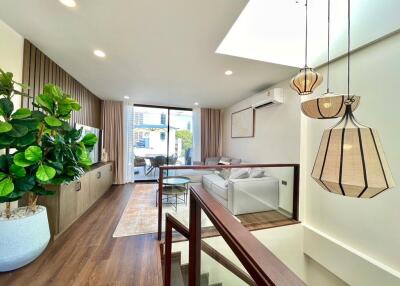 Modern living room with staircase, indoor plant, comfortable seating area, and large windows.