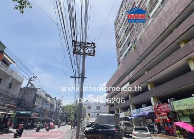 Street view of commercial and residential buildings with parked cars and pedestrians