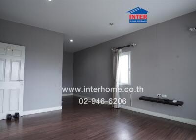 Spacious and empty living area with wooden flooring and gray walls.