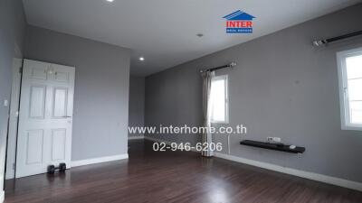 Spacious and empty living area with wooden flooring and gray walls.