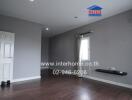 Spacious and empty living area with wooden flooring and gray walls.