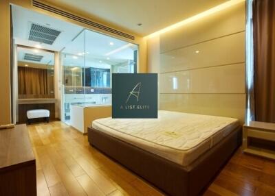 Spacious bedroom with wooden flooring and large glass-walled ensuite bathroom