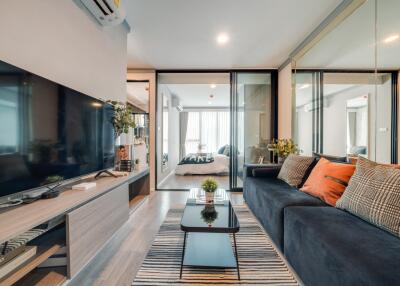 Modern living room with a TV, sofa, and glass doors leading to a bedroom