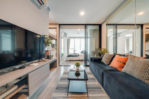 Modern living room with a TV, sofa, and glass doors leading to a bedroom