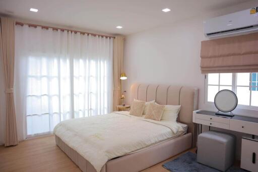 Spacious bedroom with a large bed, side table, dressing table, and air conditioner.