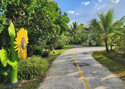 A scenic outdoor pathway surrounded by lush greenery and a sunflower sculpture