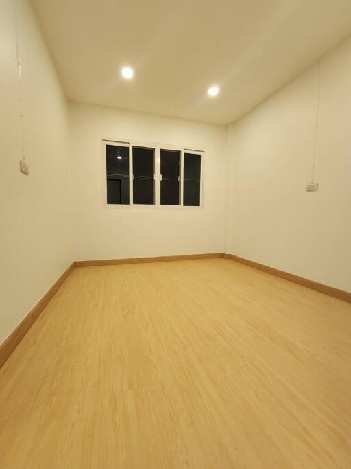 Well-lit empty bedroom with wooden floor and white walls