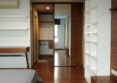 Modern bedroom with wooden flooring, shelves, and a large mirror