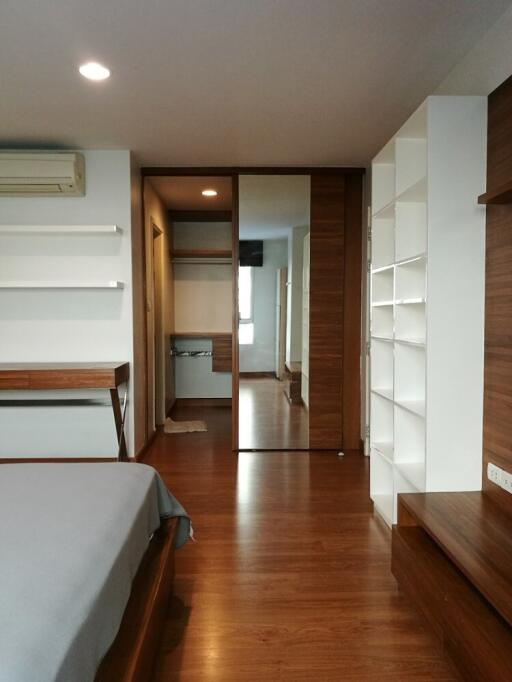 Modern bedroom with wooden flooring, shelves, and a large mirror