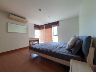 A spacious, well-lit bedroom with a comfortable bed, wooden flooring, and a wall-mounted air conditioning unit.