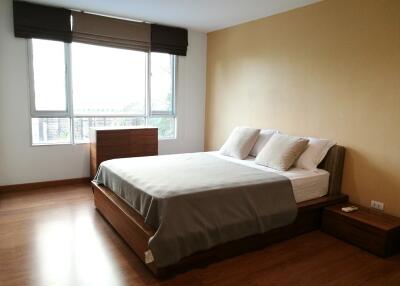 Spacious and well-lit bedroom with a large bed, side tables, window blinds, and wooden flooring