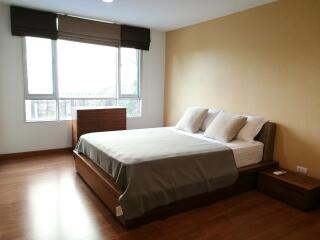 Spacious and well-lit bedroom with a large bed, side tables, window blinds, and wooden flooring