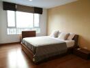 Spacious and well-lit bedroom with a large bed, side tables, window blinds, and wooden flooring