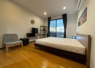 Modern bedroom with a large window overlooking the city, featuring a double bed, seating area, and entertainment setup.