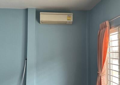 A bedroom with blue walls, an air conditioner, and a window with orange curtains