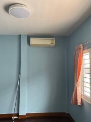 A bedroom with blue walls, an air conditioner, and a window with orange curtains