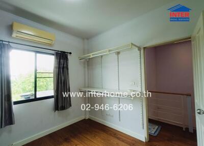 Empty bedroom with wooden floors, wall-mounted shelves, air conditioner, and a window with curtains.