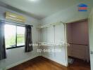 Empty bedroom with wooden floors, wall-mounted shelves, air conditioner, and a window with curtains.