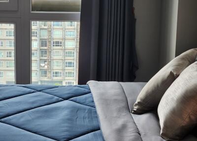 Bedroom with blue comforter and pillows, large window with city view