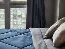 Bedroom with blue comforter and pillows, large window with city view