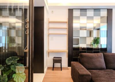 Modern living room with a brown sofa, wooden flooring, mirrors, shelving, and green plants