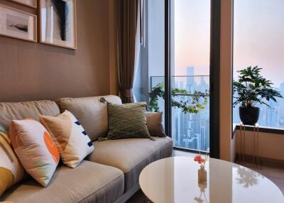 A cozy living room with a sofa, decorative pillows, and a coffee table with city view in the background and potted plants.