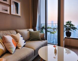 A cozy living room with a sofa, decorative pillows, and a coffee table with city view in the background and potted plants.