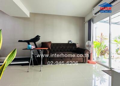 Modern living room with a brown sofa, exercise equipment, and sliding glass doors leading to an outdoor area