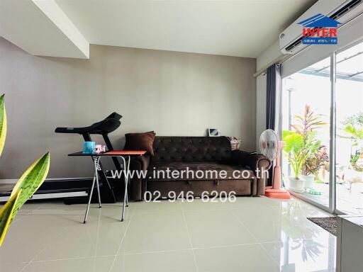 Modern living room with a brown sofa, exercise equipment, and sliding glass doors leading to an outdoor area