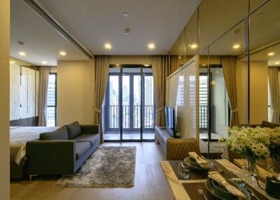 Modern apartment living room with a view of the city, featuring a couch, dining table, and large windows leading to a balcony.