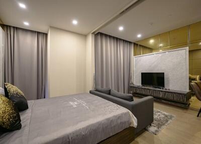 Modern bedroom with a large bed, gray bedding, a grey sofa, and a TV on the opposite wall.