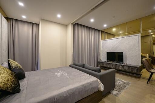 Modern bedroom with a large bed, gray bedding, a grey sofa, and a TV on the opposite wall.