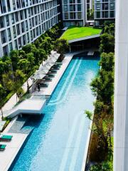 View of a modern apartment complex with a large outdoor swimming pool and sun loungers