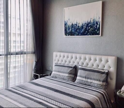 Modern bedroom with large window, artwork, and patterned bedding