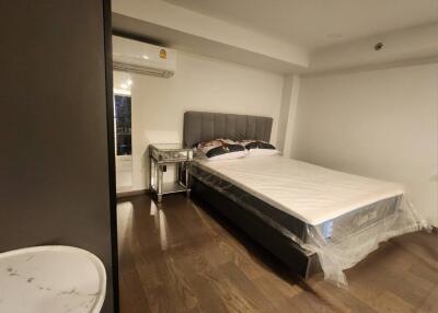 Spacious bedroom with bed, side table, air conditioner, and wooden flooring