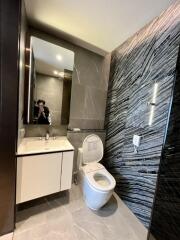 Modern bathroom with sleek design, featuring a toilet, vanity with sink, large mirror, and tiled walls