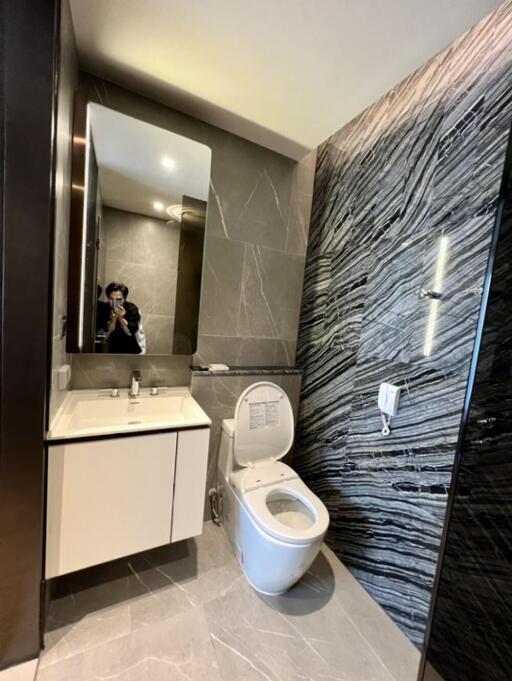 Modern bathroom with sleek design, featuring a toilet, vanity with sink, large mirror, and tiled walls