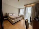 Bedroom with bed, seating area, and large windows with sheer curtains.