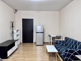 Main living area with sofa, TV stand, mini fridge, dining table, and coat rack